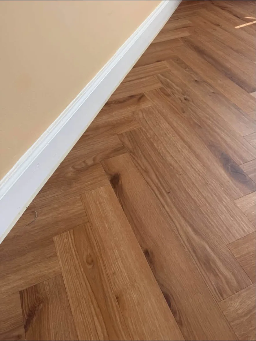 Close-up of herringbone wood-effect flooring neatly finished against white skirting